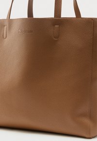 Καφέ δερμάτινη τσάντα tote με υφή, δύο χερούλια και ανάγλυφο διακριτικό όνομα μάρκας στο πάνω μπροστινό μέρος.