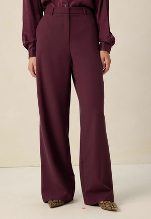 Pantalons larges bordeaux en tissu lisse avec une taille haute et une coupe ajustée, présentant un léger éclat et des lignes épurées.