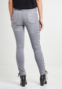 Šedé skinny džíny s šněrováním na vnějších švech, vázáním na kotnících a hladkou denimovou strukturou. Design s pěti kapsami.
