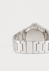 Relógio de metal prateado com bracelete de aço inoxidável. Caixa redonda com detalhe na coroa, fundo plano e logótipo gravado na fivela.