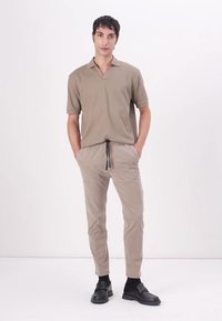 Beige polo shirt with a V-neck and short sleeves, paired with light beige tapered pants and black slip-on shoes with a smooth finish.