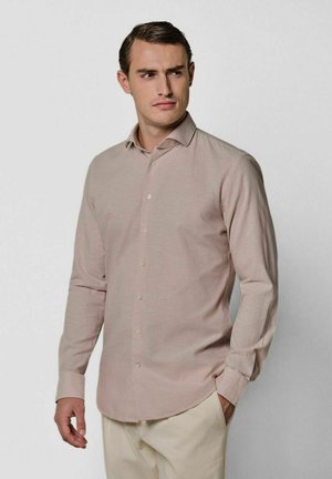 Camisa de manga larga de color rosa claro con botones, que presenta un cuello abierto, una textura sutil y un dobladillo recto. Combinada con pantalones crema.