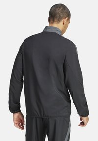 Giacca sportiva nera con una texture liscia, dettagli grigi sul colletto e sulle spalle, e maniche lunghe. Presenta un design aderente per garantire mobilità.