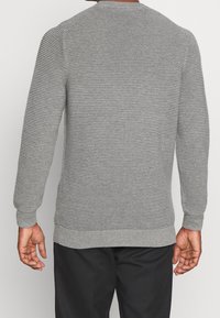 Grå strikket sweater med horisontal ribbet tekstur, rund halsudskæring, lange ærmer og tætsiddende manchetter og kant.