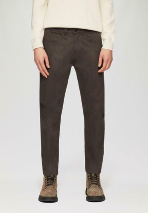 Bruine, slim-fit broeken van gladde stof, met zijzakken en knoopsluiting. Gecombineerd met beige laarzen voor contrast.