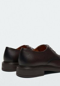 Chaussures en cuir marron avec une finition texturée, bout arrondi et semelle en caoutchouc épaisse. Présente des lacets et des détails de couture subtils.