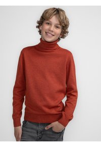 Maglione a collo alto rosso realizzato in tessuto lavorato a maglia, con scollatura e polsini a costine, abbinato a jeans scuri. Tessuto morbido e vestibilità comoda.
