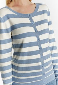 Lätt cardigan gjord av mjukt tyg, med horisontella blå och vita ränder, rund halsringning och blå knappar framtill.