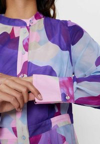Genomskinlig blus i lila, rosa och blå abstrakt mönster. Mjuk tyg med knappp detaljer fram och vid manschetterna. Långa ärmar.