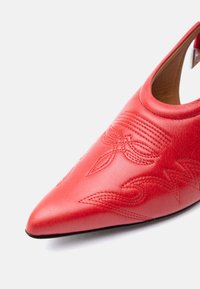 Κόκκινο δερμάτινο παπούτσι με μυτερή μύτη και περίπλοκα κεντημένα λουλουδένια και κυματιστά σχέδια στην κορυφή.