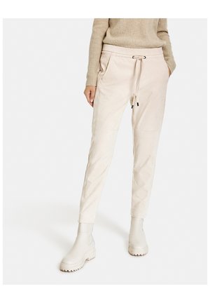 Pantalon beige à cordon de serrage assorti à de grosses bottes et un pull en tricot marron clair, présenté de la taille aux pieds.