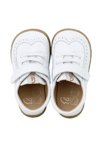Zapatos de cuero blanco con una forma suave y redondeada, que cuentan con perforaciones decorativas y una correa de velcro. Suelas de goma marrón para un mejor agarre.