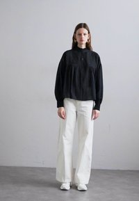 Black textured blouse with buttons and long sleeves, paired with white wide-leg jeans and white sneakers. Simple design with subtle details.