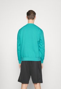 Sudadera turquesa con cuello redondo y mangas largas, combinada con pantalones cortos negros. La tela parece suave, con puños y dobladillo acanalados.