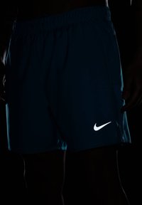 Tummansiniset Nike-shortsit, joissa on elastinen vyötärö, sivutaskut ja heijastava valkoinen Nike-logo oikeassa alakulmassa.