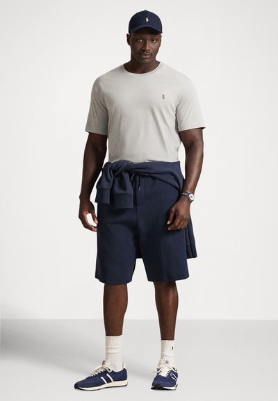 Ανοιχτό γκρι μπλουζάκι, σκούρο μπλε σορτς, και μπλε αθλητικά παπούτσια. Μπλούζα δεμένη στη μέση, με άσπρες κάλτσες και σκούφο σε σκούρο μπλε. Απλός σχεδιασμός και άνετη εφαρμογή.