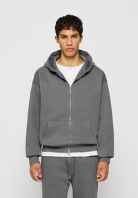 Grauer Zip-Hoodie aus weichem Material, mit einer großen Kapuze, Fronttaschen, gerippten Bündchen und einem weißen Saumdetail.