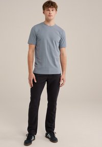 Camiseta de manga corta azul claro con cuello redondo, combinada con pantalones negros y zapatillas oscuras con rayas blancas. Textura suave.