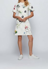 Kortärmad vit klänning med ett blommönster i olika färger, med en avslappnad passform och rund halsringning, kombinerad med vita sneakers.