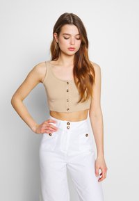 Top cropped em tom bege com textura canelada, apresentando um decote redondo e cinco botões na parte da frente. Combinado com calças brancas de cintura alta com detalhes em botões dourados.