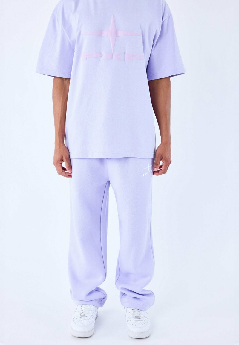 Maglietta di cotone lavanda con logo rosa lucido, abbinata a pantaloni larghi coordinati. Sneakers bianche completano l'outfit.