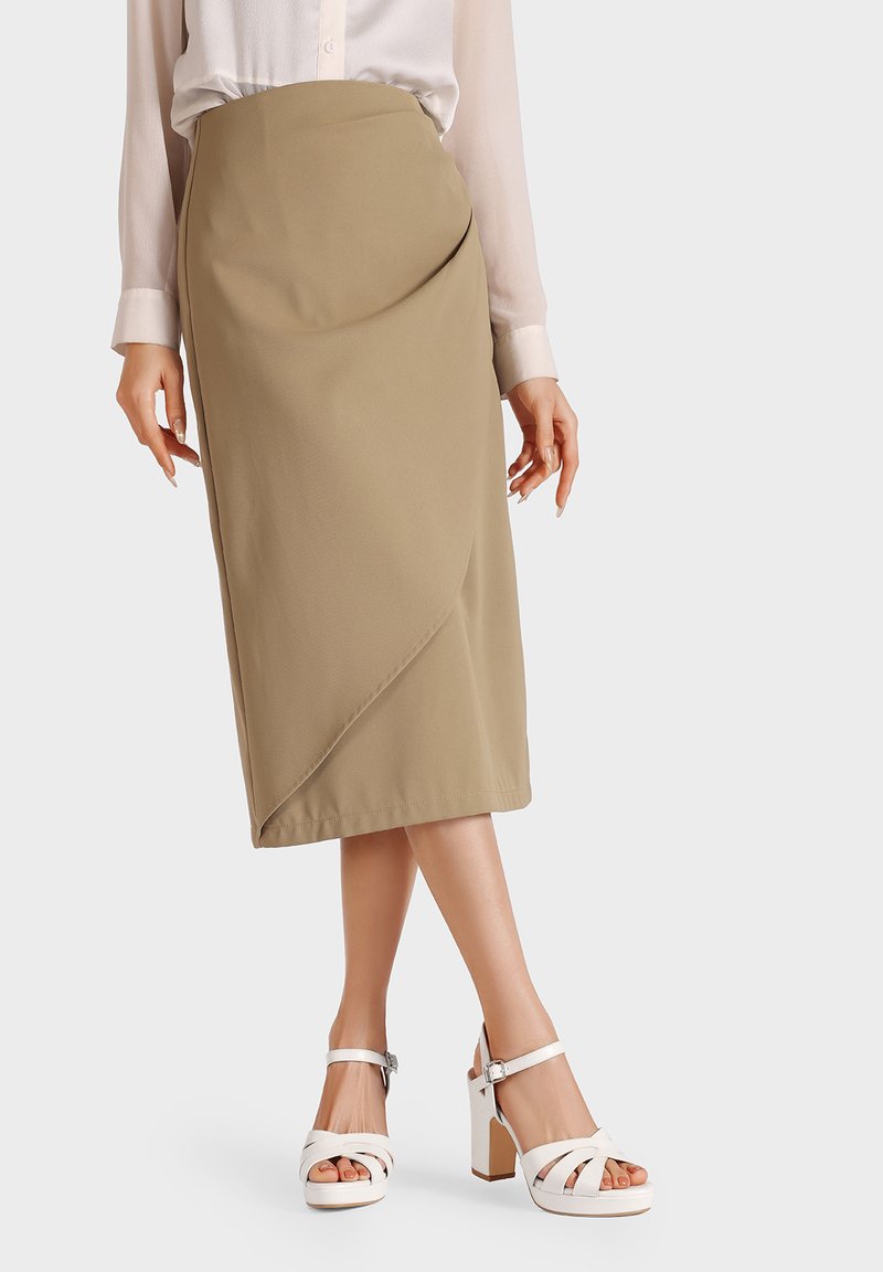 Gonna beige di lunghezza ginocchio con design drappeggiato, texture liscia e orlo curvato sottile. Abbinata a sandali bianchi con tacco blocco e cinturini.