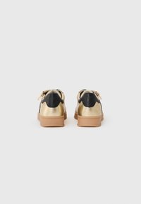 Sneaker neri e oro con una tomaia metallica liscia, suola in gomma e dettaglio sul tallone a contrasto; presenta accenti con zip sui lati.