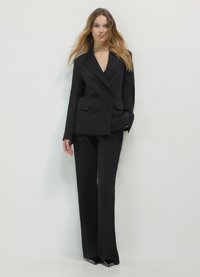 Costume noir à double boutonnage avec des revers crantés, un pantalon large et des détails subtils aux poches. Tissu lisse avec une coupe ajustée. Sans motifs ni ornements.