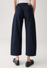 Brede donkerblauwe spijkerbroek met hoge taille, met twee achterzakken en een tan leren label op de tailleband.