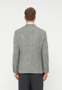 Szary, kraciasty żakiet o dopasowanym kroju, z wyrazistymi klapami i teksturowanym materiałem. Zawiera dwa rozcięcia z tyłu i mankiety zapinane na guziki.