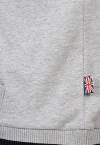 Grå sweatshirt med struktureret stof, sidelomme og et lille Union Jack mærke ved kanten. Ribbet manchet nederst.