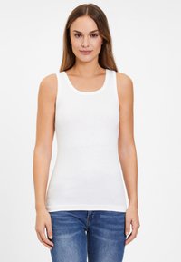 Weißes Baumwolltop ohne Ärmel mit gerippter Textur, runder Ausschnitt und gewellten Kanten. Getragen mit blauen Jeans. Verfügt über ein tailliertes Design.