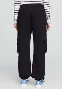 Czarne dresy z kieszeniami cargo po bokach, elastycznym pasem i szerokimi nogawkami. Noszone z paskowanym, długim rękawem i niebieskimi trampkami.