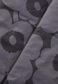 Tissu gris avec un grand motif floral foncé au toucher lisse. Le design comprend des pétales qui se chevauchent et des formes circulaires.