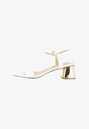 Sandal blanco con dos correas anchas y una correa en el tobillo con hebilla. Presenta un tacón cuadrado con acentos dorados. Textura suave en toda la superficie.