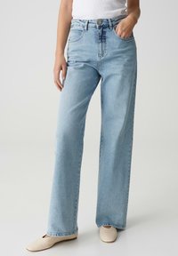 Light blue wide-leg jeans made from denim, featuring a high waist, front pockets, and subtle fading. Paired with light-colored flats.