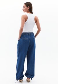 Siniset farkut leveällä lahkeella, joissa on rento istuvuus, sivutaskut, nyöripohjat ja keskikorkea vyötärö. Yhdistetty valkoiseen hihattomaan puseroon.