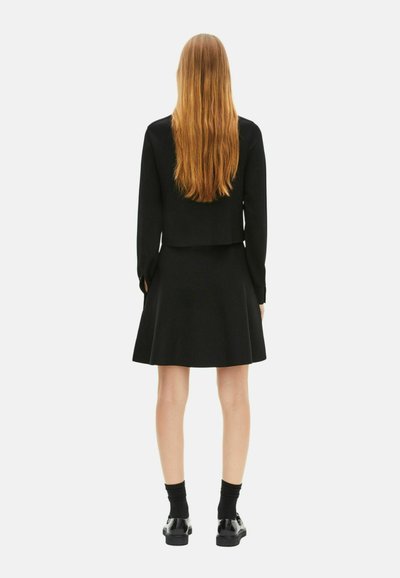 Zwarte cropped jack gecombineerd met een zwarte rok. De outfit heeft lange mouwen en een uitlopende rok. Glamoureuze zwarte schoenen maken de look compleet.
