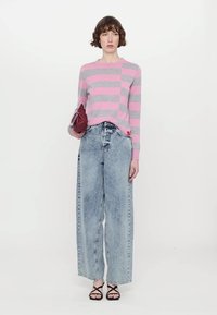 Striped pink and gray sweater, light denim wide-leg jeans, and black strappy sandals. Model holds a burgundy clutch bag.