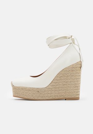 White wedge heel shoe with a rounded toe and ankle strap, featuring a textured jute platform and smooth leather upper.