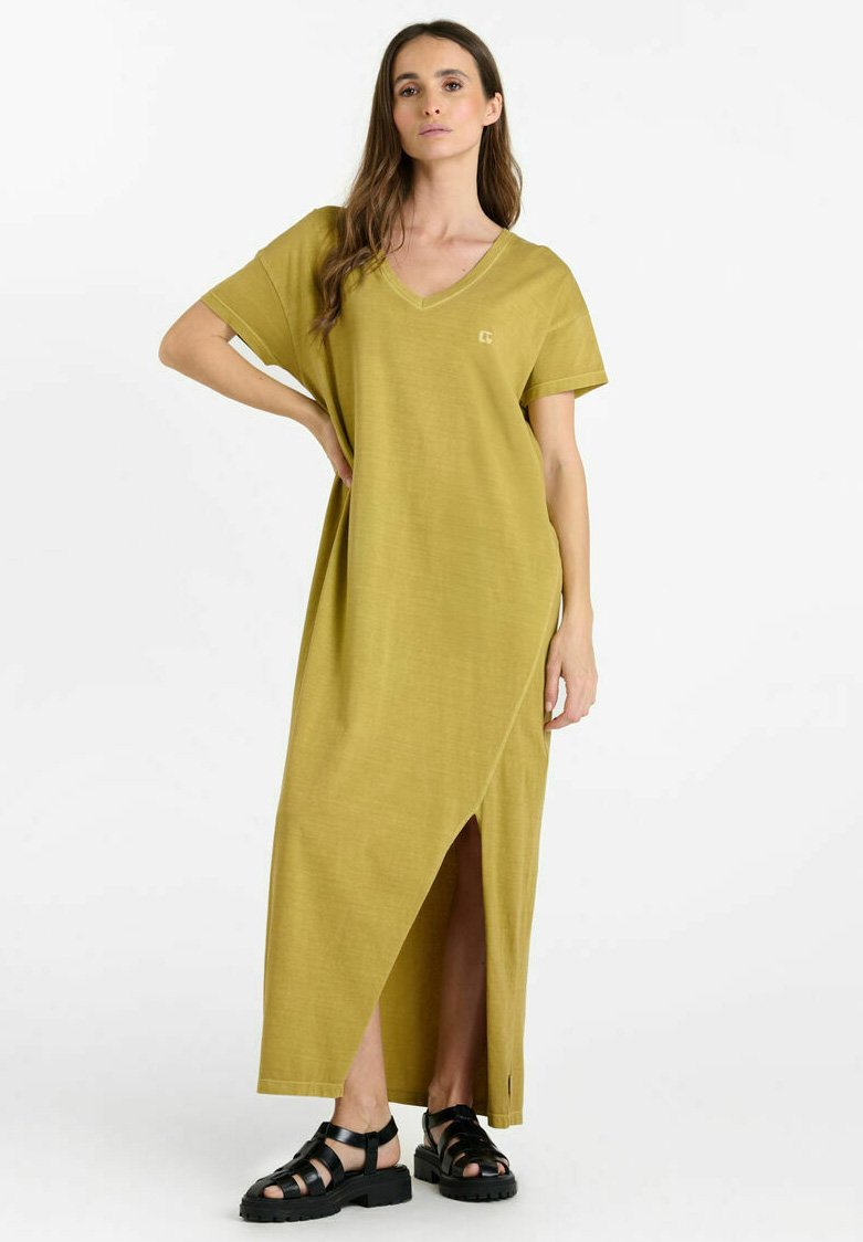 Olijfgroene maxi jurk met V-hals, korte mouwen en een zijsplit, voorzien van logo-detail. Gecombineerd met zwarte, gestrikte sandalen. Gladde stofstructuur.