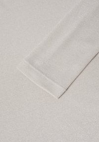 Tessuto di maglia grigio chiaro con una leggera lucentezza; presenta un risvolto su una superficie liscia e texture.
