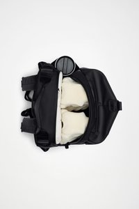 Czarny plecak z regulowanymi paskami, otwierany od góry; w środku znajdują się białe wyściełane przedmioty. Na zewnątrz gładki materiał i okrągła kieszeń.