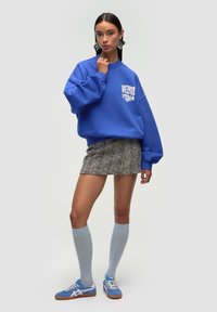 Sudadera azul de gran tamaño con gráfico, falda de tweed texturizado, calcetines hasta la rodilla de color azul claro y zapatillas azules con acentos blancos.