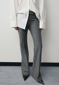 Sive krojene hlače s razširjenim krojem, značilne po gladki teksturi. Ujemajo se z belo oversize srajco z gumbi in točkastimi črnimi petami.