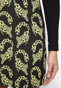 Robe en maille présentant un tissu noir orné de motifs léopard jaunes, avec des têtes de léopards bondissant et des queues courbées.