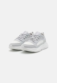 Szare i białe buty sportowe z siateczkowymi panelami, zaokrąglonym czubkiem, sznurowanym przodem, wyściełanym kołnierzem i teksturowaną podeszwą. Zawierają subtelny detal z logo.