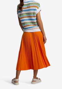 Virkattu yläosa monivärisillä raidoilla, yhdistetty oranssiin plissoonihameeseen. Valkoiset lenkkarit, joissa koristeelliset rusetit, viimeistelevät asun.