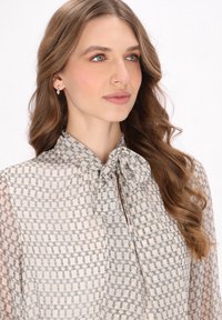 Lichtgekleurde blouse met een geplooide strikboord, voorzien van een geometrisch patroon in donkere lijnen. Gemaakt van doorschijnende stof met een zachte textuur.