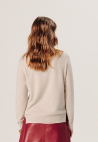 Helle beigefarbene Sweater aus weichem Material, mit einem runden Halsausschnitt, langen Ärmeln und einem gerippten Saum, kombiniert mit einem roten Lederrock.